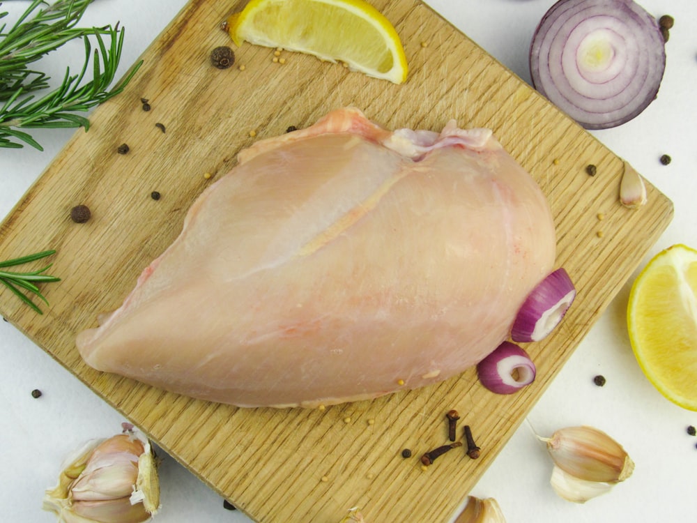 a raw chicken on a cutting board with garlic, lemon, and garlic