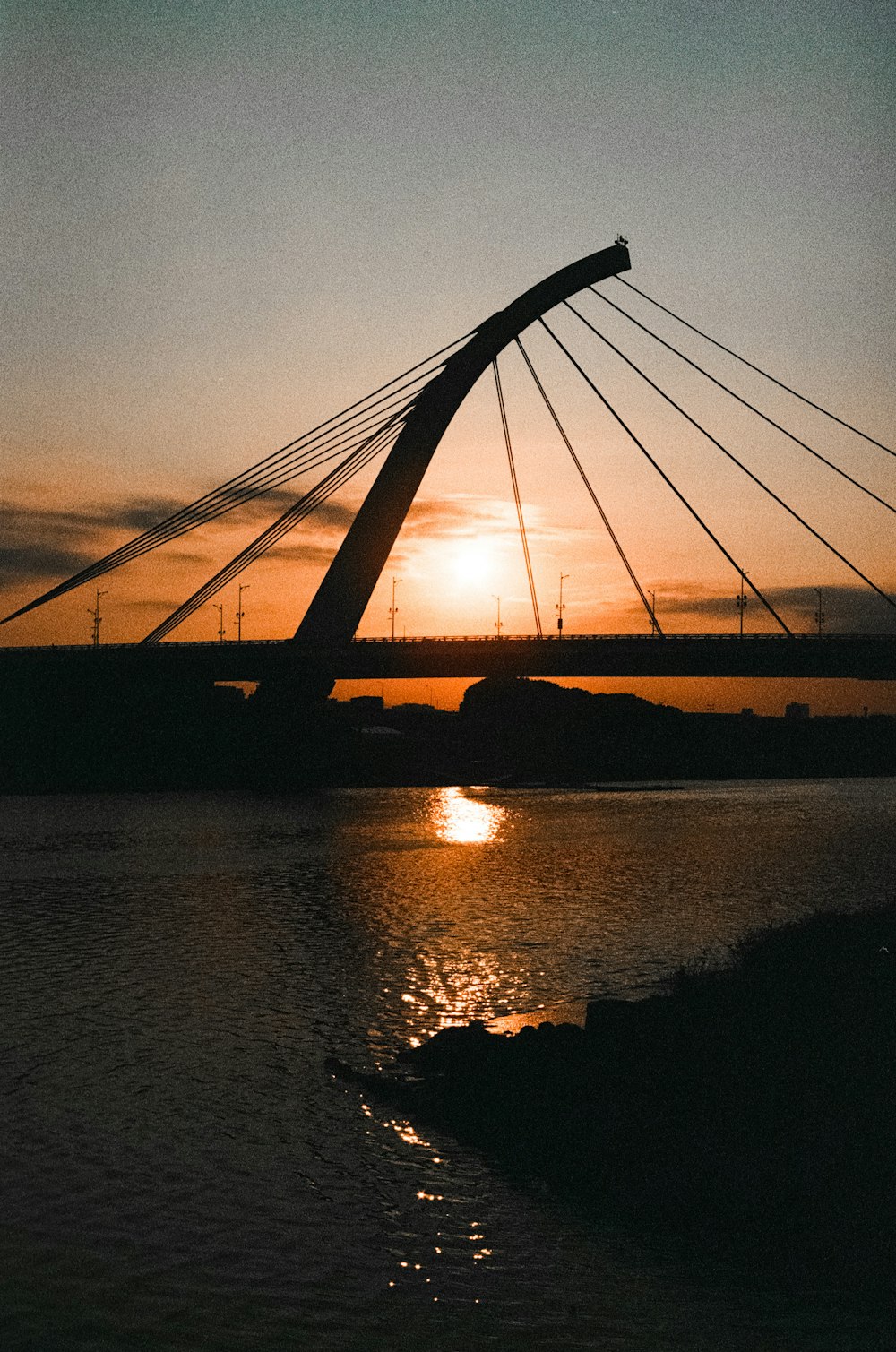 the sun is setting over a bridge over a body of water