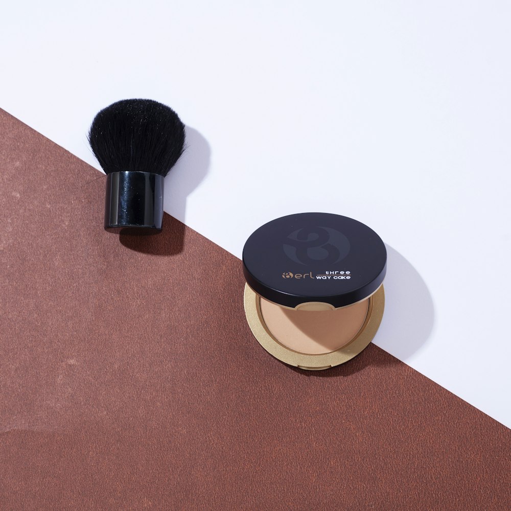a makeup brush and compact foundation on a brown and white background