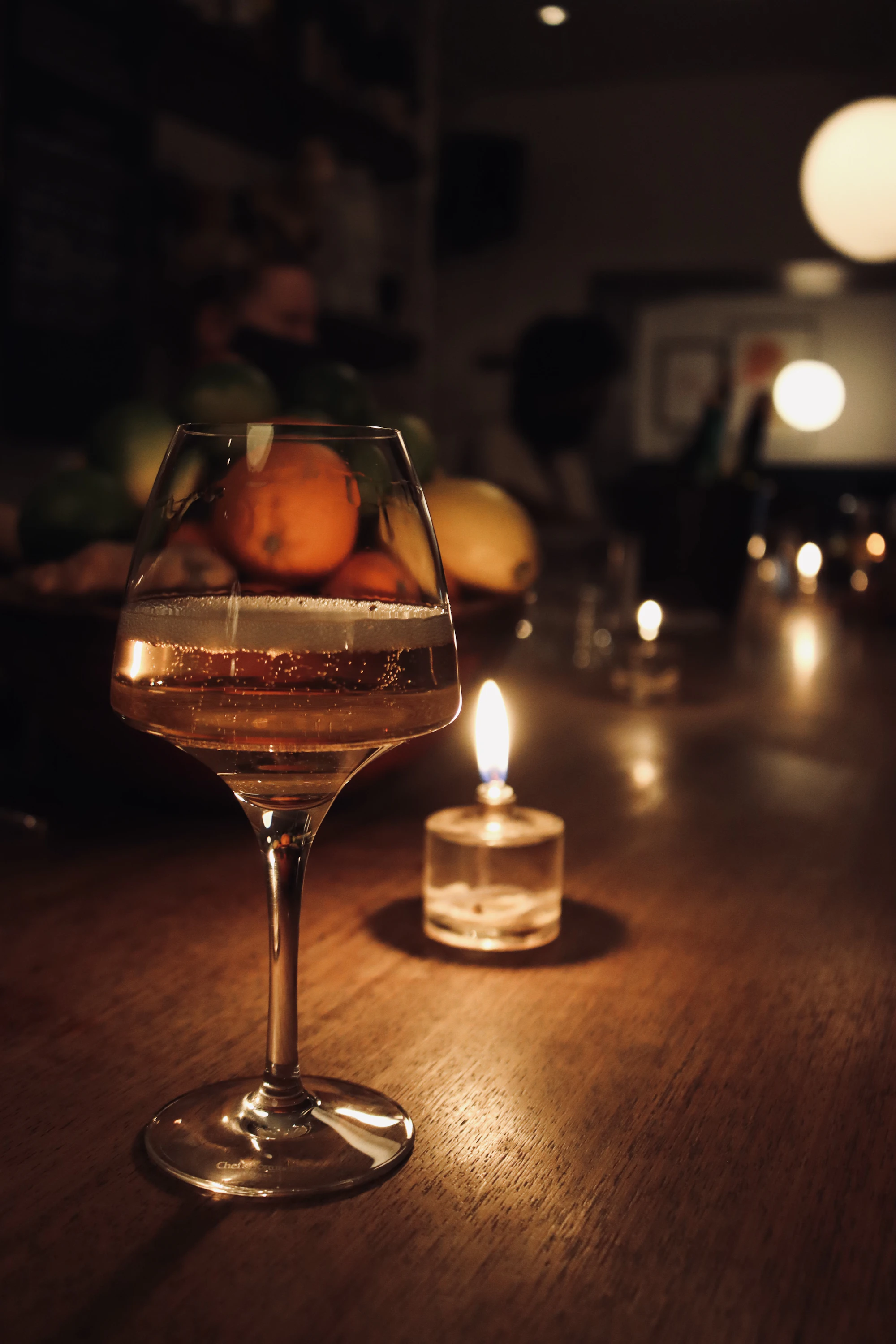 A glass of red wine next to a lit candle on a dark table