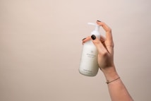 A hand with dark nail polish holds a white bottle labeled 'everdrop natural care' with a pump dispenser. The background is plain and neutral-colored.