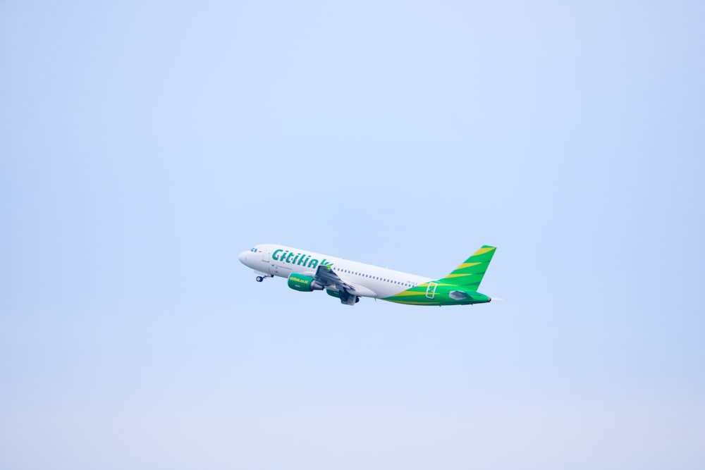 a green and white jet airliner flying in the sky