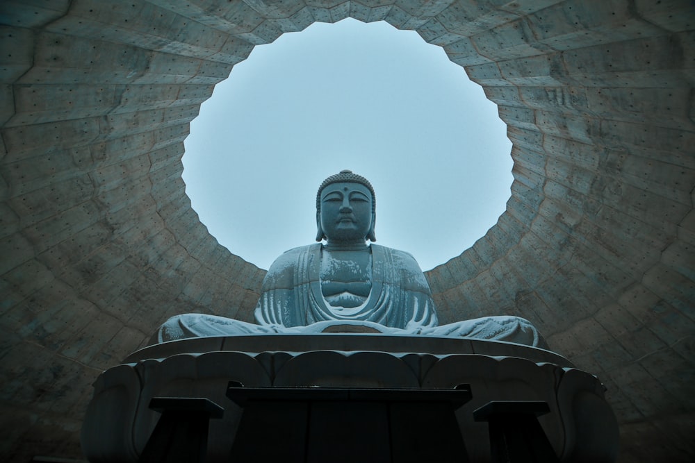 a buddha statue sitting in front of a round window