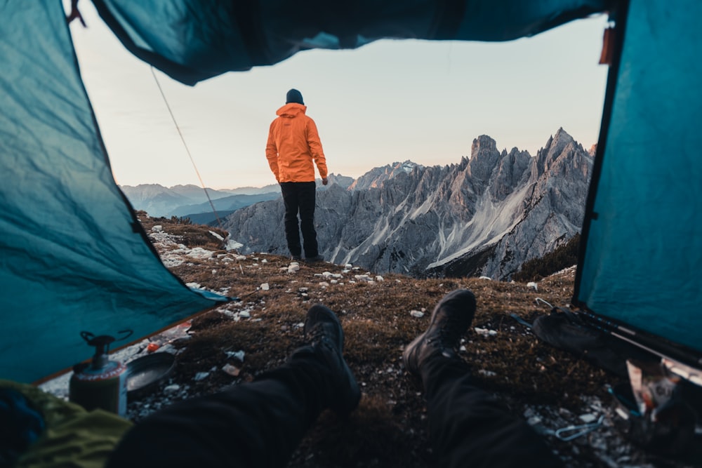 a man in an orange jacket standing in front of a tent