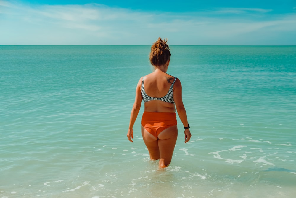 a woman in a bikini walking into the ocean