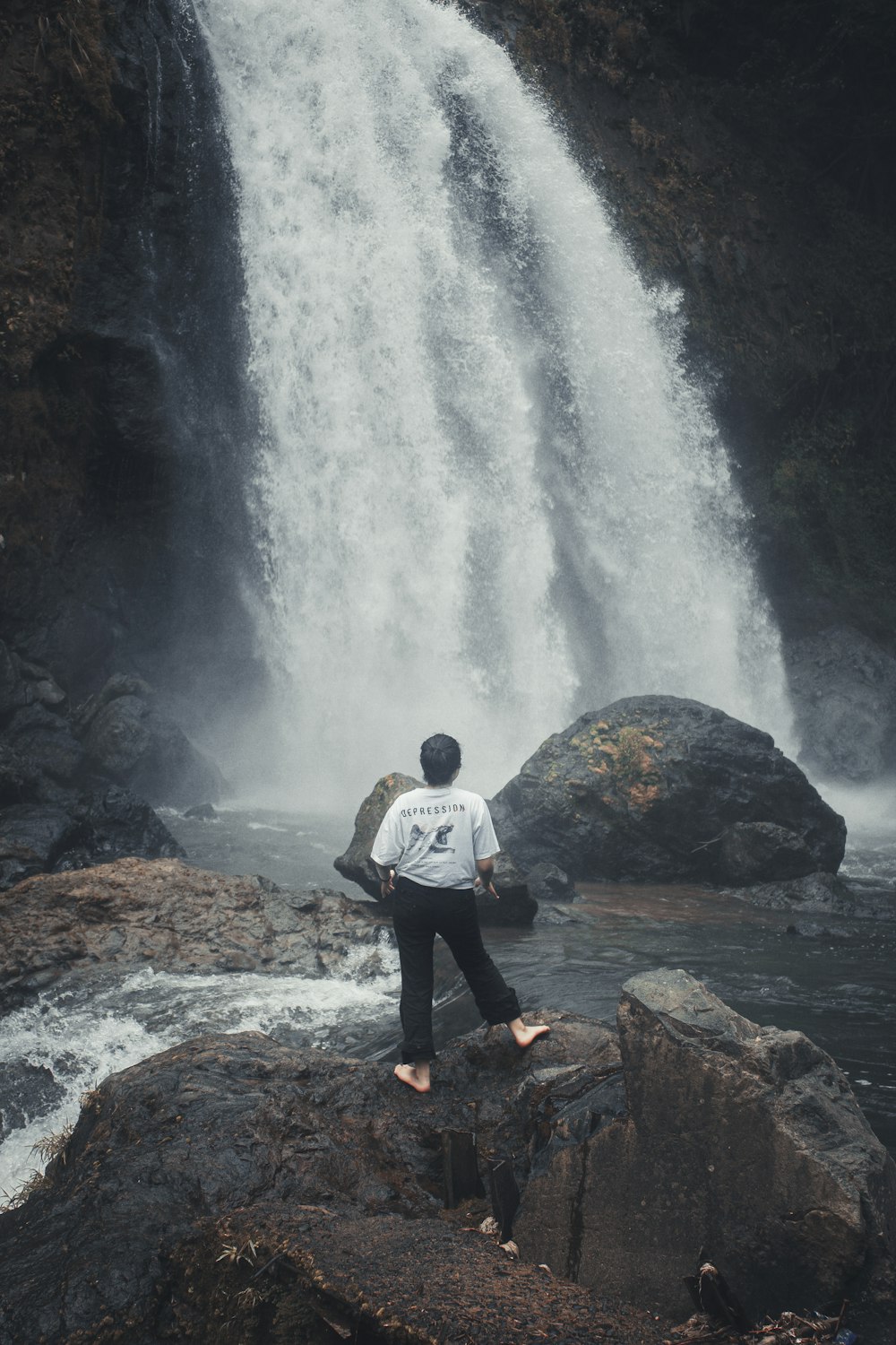 a man standing on a rock in front of a waterfall