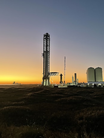 Starry night sky with a faint silhouette of a rocket standing tall on the launchpad, ready for liftoff