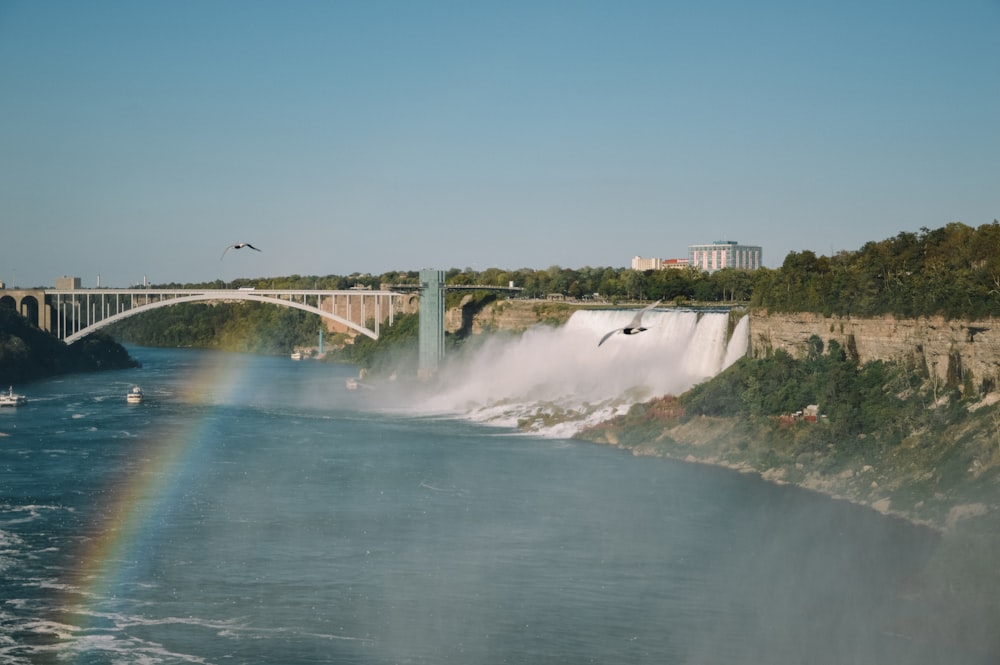 a rainbow in the sky over a waterfall and a bridge