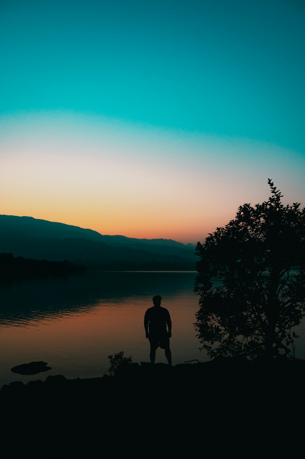 a man standing on the shore of a lake at sunset