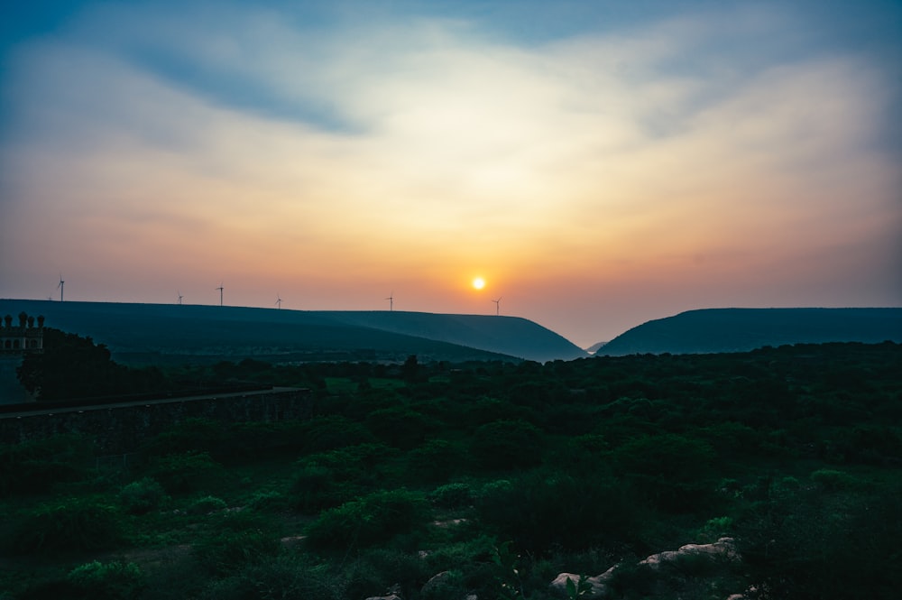 the sun is setting over the hills in the distance