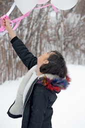 a young boy holding a bunch of balloons in the snow