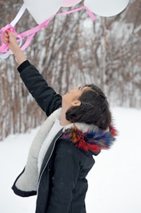 a young boy holding a bunch of balloons in the snow