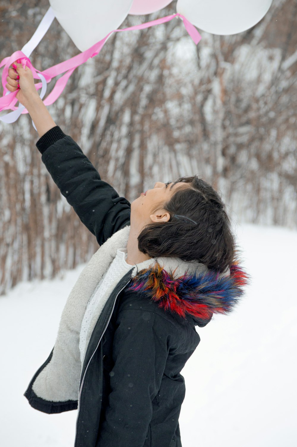 a young boy holding a bunch of balloons in the snow