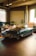 A classic convertible car is parked inside a spacious workshop. The vehicle has a sleek design with a dark green color. There are cardboard boxes and various tools scattered around, suggesting a space used for automotive repair or restoration. Large windows allow natural light to enter, illuminating the tiled floor and giving a warm ambiance.