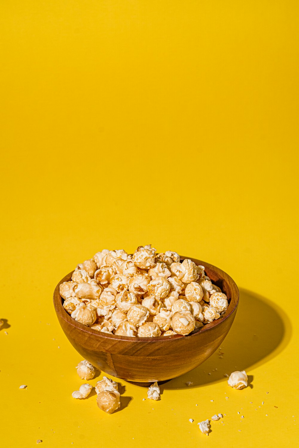 a wooden bowl filled with popcorn on a yellow background