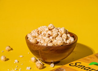 a wooden bowl filled with popcorn next to a bag of peanuts