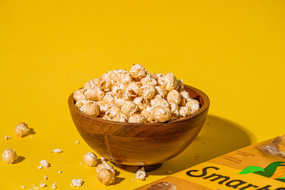 a wooden bowl filled with popcorn next to a bag of peanuts