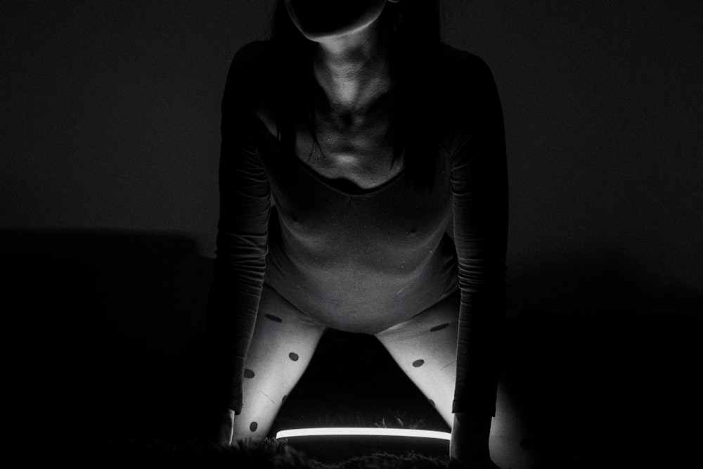 une femme agenouillée dans le noir, les mains sur les genoux