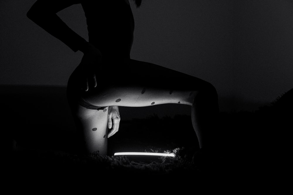Une femme debout dans le noir, les jambes croisées
