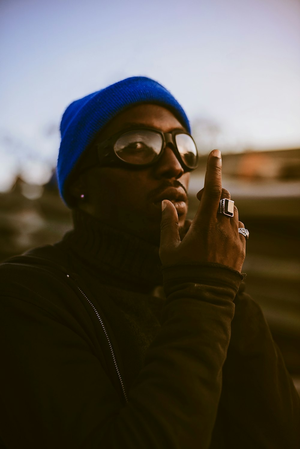 a man wearing glasses and a beanie smoking a cigarette