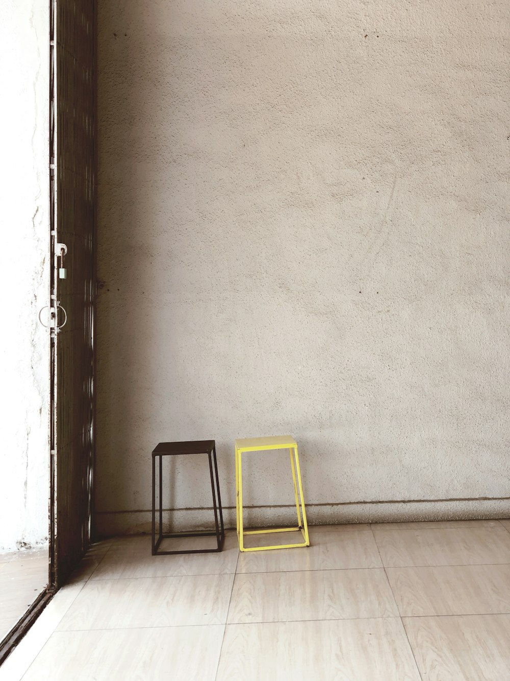 a yellow chair and a black stool against a white wall