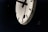 A large, round wall clock with a minimalist design is visible. It features bold black hour and minute hands against a white background, with black notches indicating hours and minutes. The image is partially dark, emphasizing the clock face.