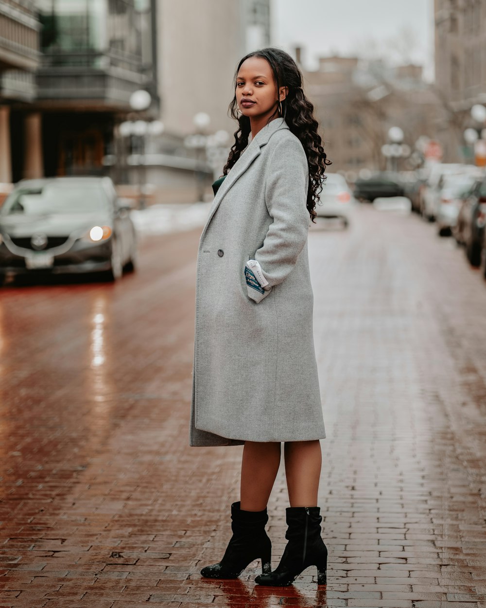 a woman standing on a brick sidewalk in a coat