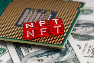 Red blocks with the letters NFT written on them are placed on a computer chip, overlaid on US dollar bills.