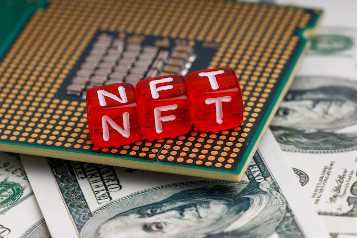 Red blocks with the letters NFT written on them are placed on a computer chip, overlaid on US dollar bills.