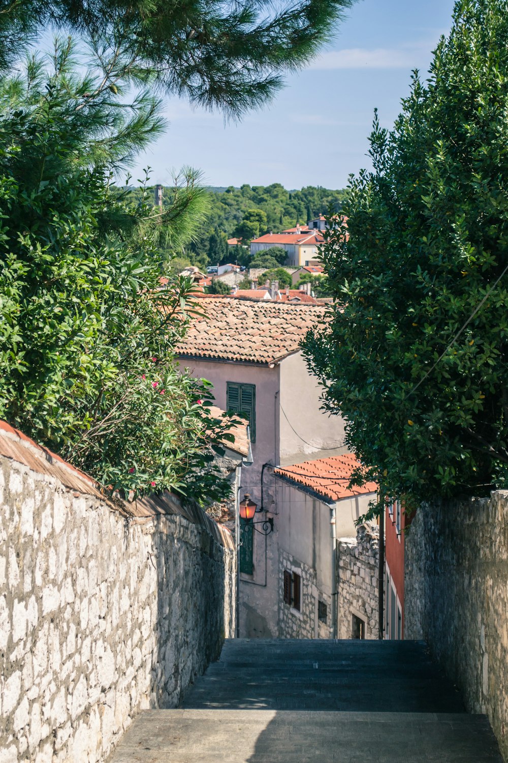 a narrow street with a stone wall and trees