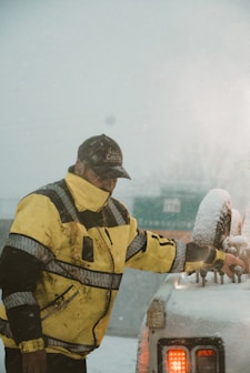 a man in a yellow jacket standing next to a car covered in snow