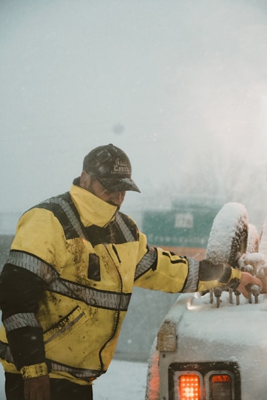 a man in a yellow jacket standing next to a car covered in snow