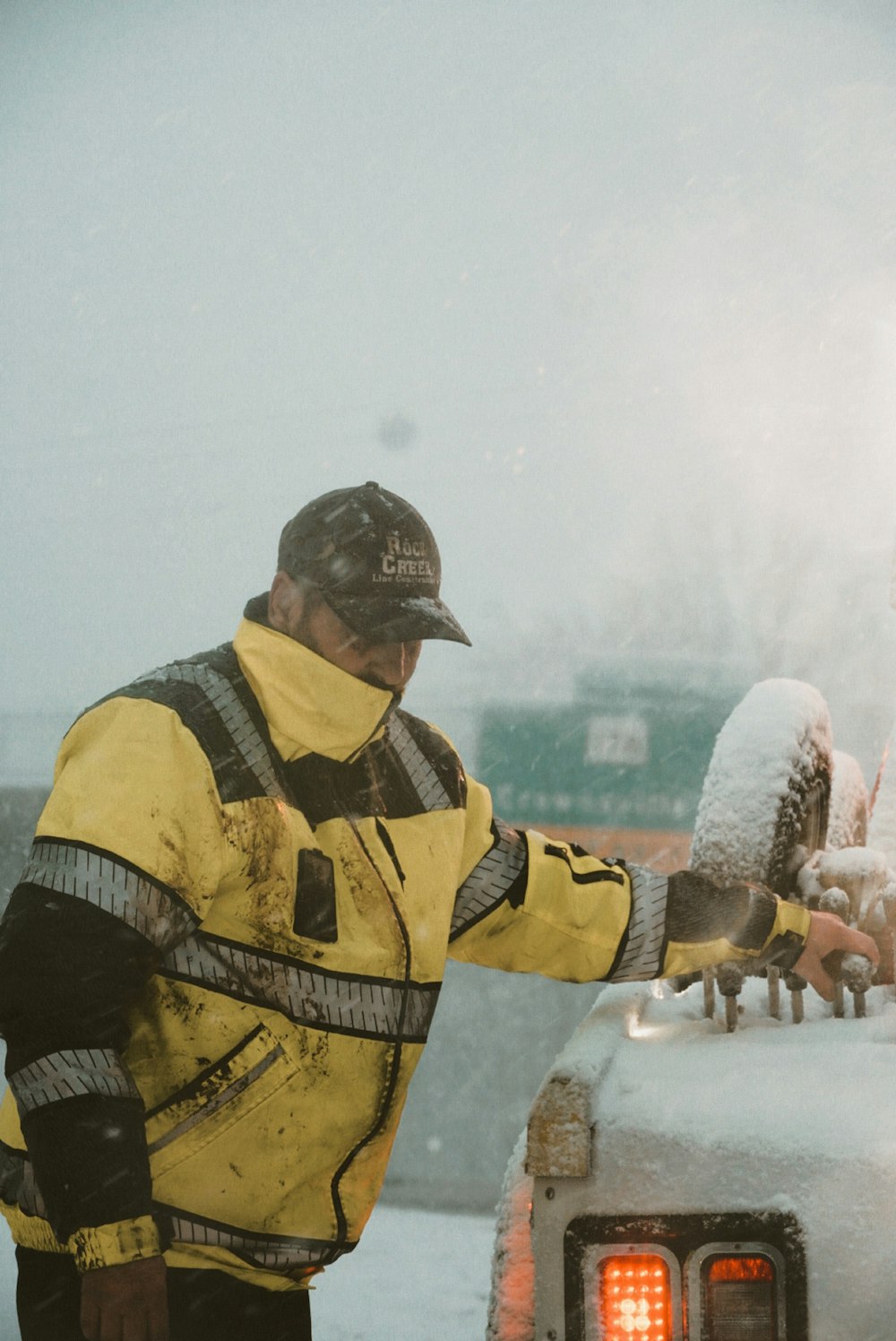 a man in a yellow jacket standing next to a car covered in snow