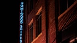 A nighttime view of a building with illuminated signage reading 'Homewood Suites' in blue neon. The building features a brick facade and multiple windows.