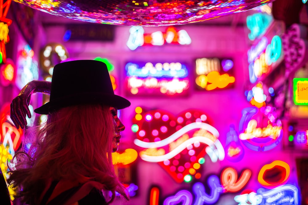 a woman wearing a top hat standing in front of neon lights