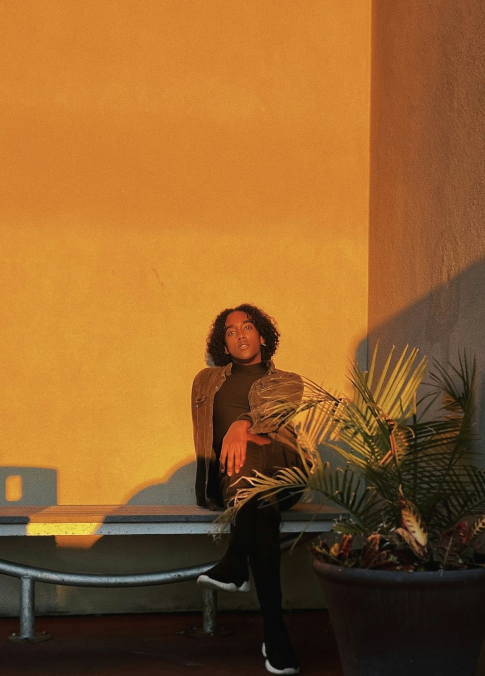 a woman sitting on a bench next to a potted plant