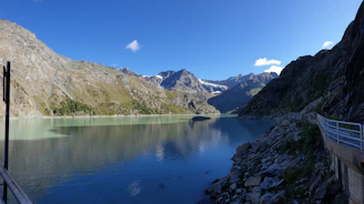 A serene mountain lake reflecting the towering slopes of Kilimanjaro, framed by rocky outcrops and clear blue sky.