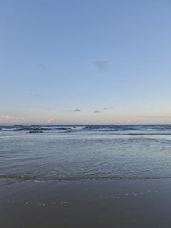 A serene ocean view with gentle waves lapping at a sandy shore under a bright blue sky.