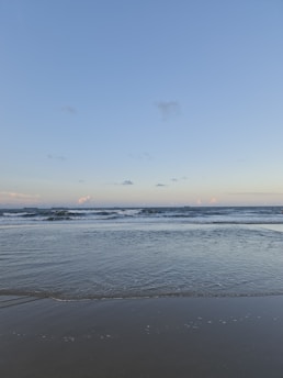 A serene ocean view with gentle waves lapping at a sandy shore under a bright blue sky.