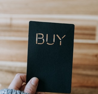 a person holding up a black book with the word buy written on it