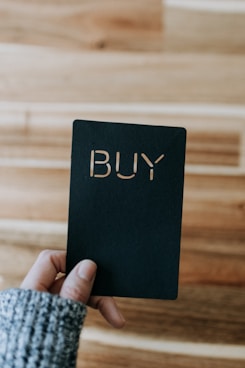 a person holding up a black book with the word buy written on it