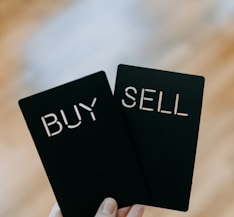 a hand holding two black cards with the words buy and sell written on them