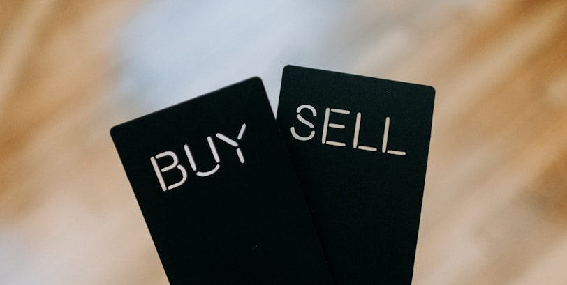 a hand holding two black cards with the words buy and sell written on them