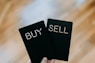 a hand holding two black cards with the words buy and sell written on them