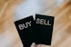 a hand holding two black cards with the words buy and sell written on them