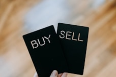 a hand holding two black cards with the words buy and sell written on them