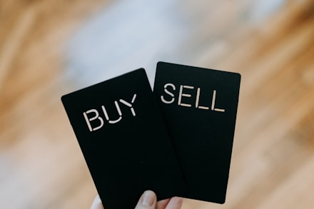 a hand holding two black cards with the words buy and sell written on them
