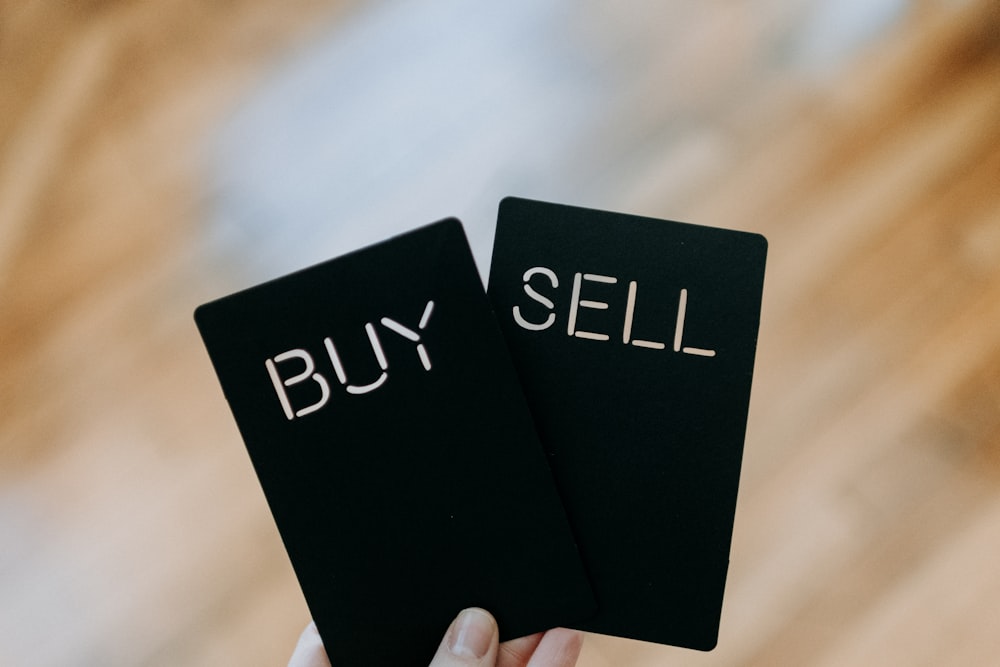 구매 및 판매라는 단어가 적힌 두 개의 검은색 카드를 들고 있는 손
