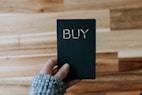 a person holding a black book with the word buy written on it