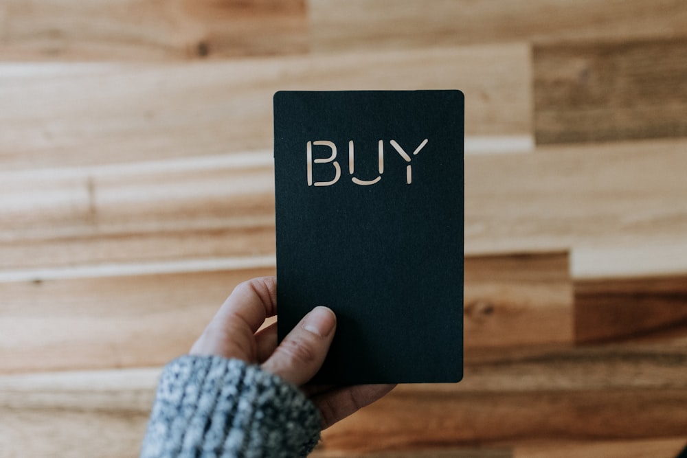 a person holding a black book with the word buy written on it